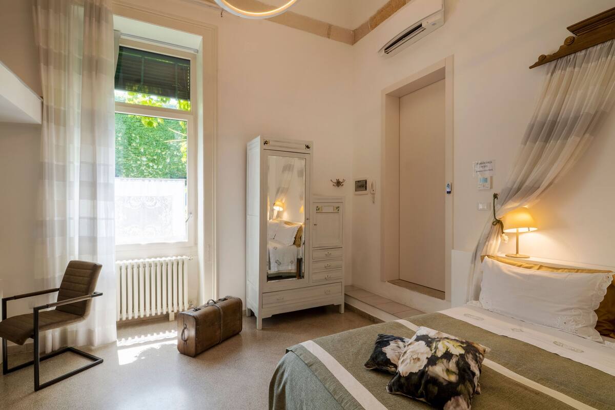 A bedroom with a bed, a chair, a dresser, a radiator, and a window with curtains.
