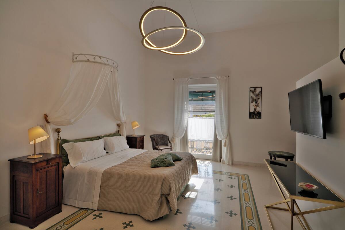 A bedroom with a bed, bedside tables, a TV, and a window with curtains.