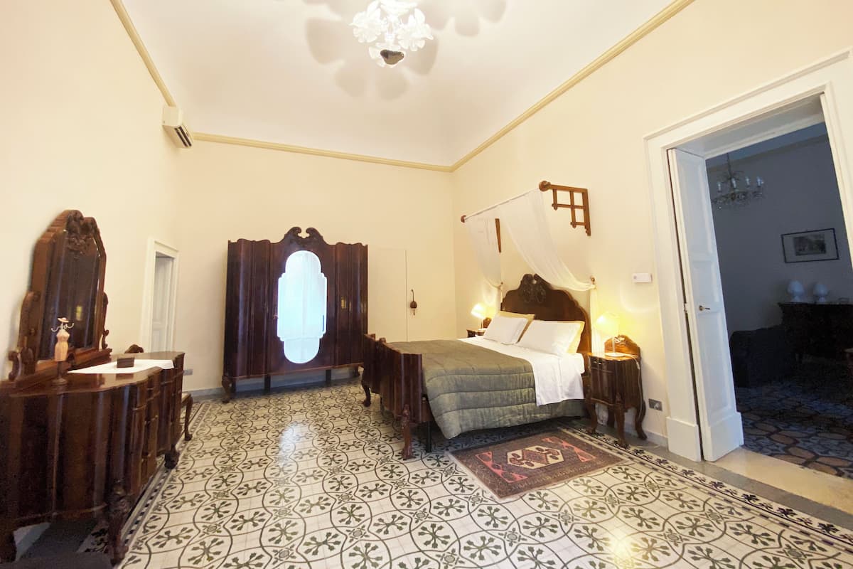 A bedroom with a four-poster bed, a wooden dresser, a mirror, and a patterned floor.