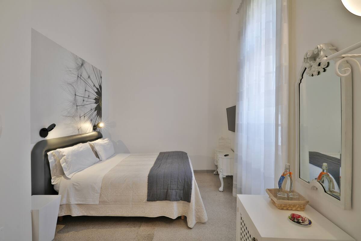 A neatly arranged bedroom with a bed, bedside table, and a large mirror.
