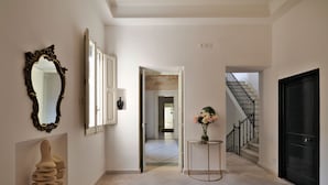 A hallway with a mirror, a sculpture, a vase with flowers, and a staircase leading to a door. - Palazzo Rollo (Lecce)