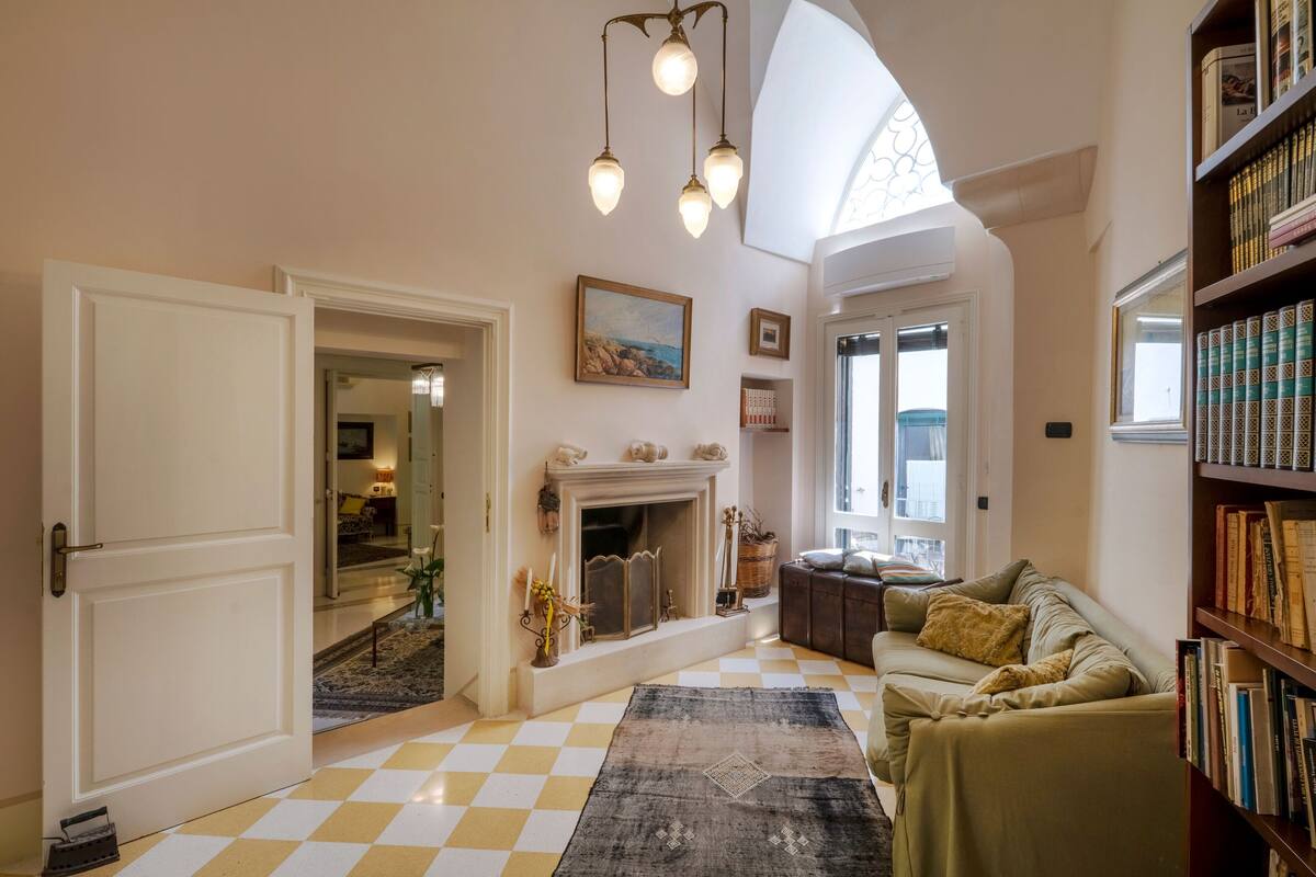 A cozy living room with a checkered floor, a fireplace, a sofa, and a bookshelf.