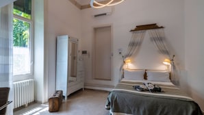 A bedroom with a bed, bedside lamps, a wardrobe, a radiator, and a window with curtains. - Palazzo Rollo (Lecce)