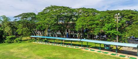 A park with a covered walkway, benches, and trees.