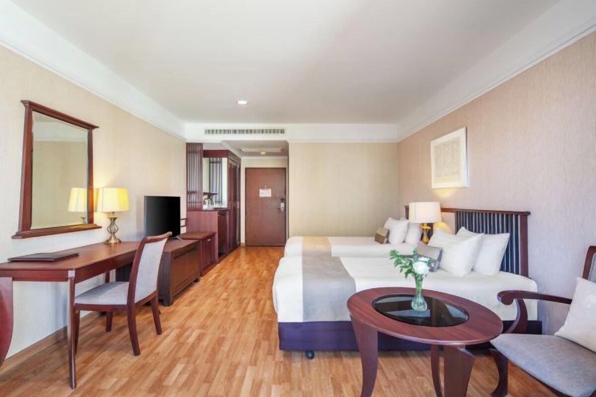 Ein Hotelzimmer mit einem Bett, einem Schreibtisch, einem Stuhl, einem Fernseher und einem kleinen Tisch mit einer Lampe.