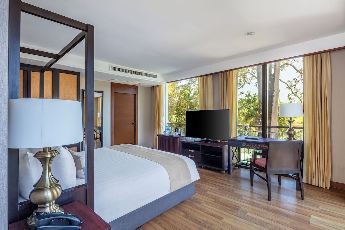Ein Hotelzimmer mit einem großen Bett, einem Schreibtisch mit Fernseher und einem Balkon mit Vorhängen.