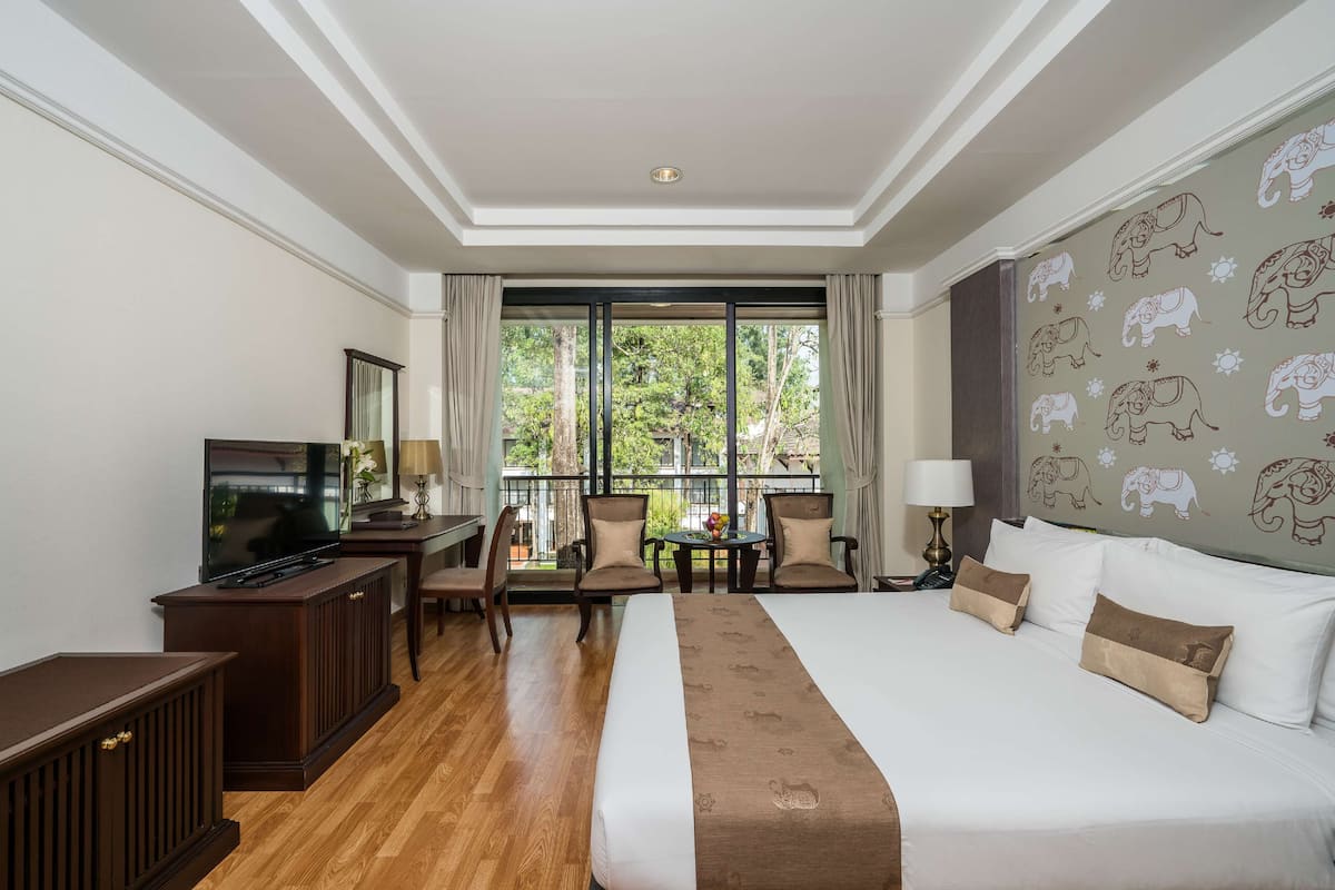 Ein Hotelzimmer mit einem großen Bett, einem Fernseher, einem Schreibtisch mit Stuhl und einem Balkon mit Blick auf Grünflächen.