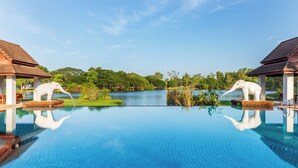 A clear blue infinity pool with two elephant statues on either side, surrounded by lush greenery and a calm lake. - Tawa Ravadee Resort, WorldHotels Distinctive (Si Maha Phot)