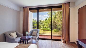 A hotel room with a bed, two armchairs, a small table, and a view of the outdoors through large windows.