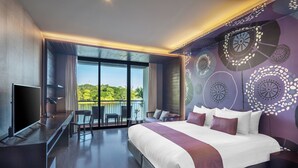 A modern hotel room with a large bed, a TV, a balcony with a view of greenery, and a patterned wall. - Tawa Ravadee Resort, WorldHotels Distinctive (Si Maha Phot)