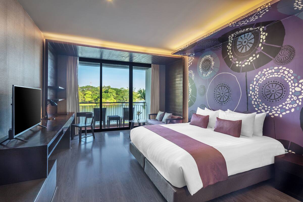 Ein modernes Hotelzimmer mit einem großen Bett, einem Fernseher, einem Balkon mit Blick auf Grünflächen und einer Wand mit Muster.