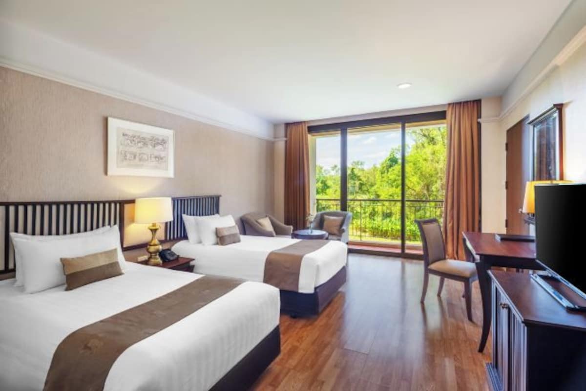 A hotel room with two beds, a desk, a chair, and a TV.