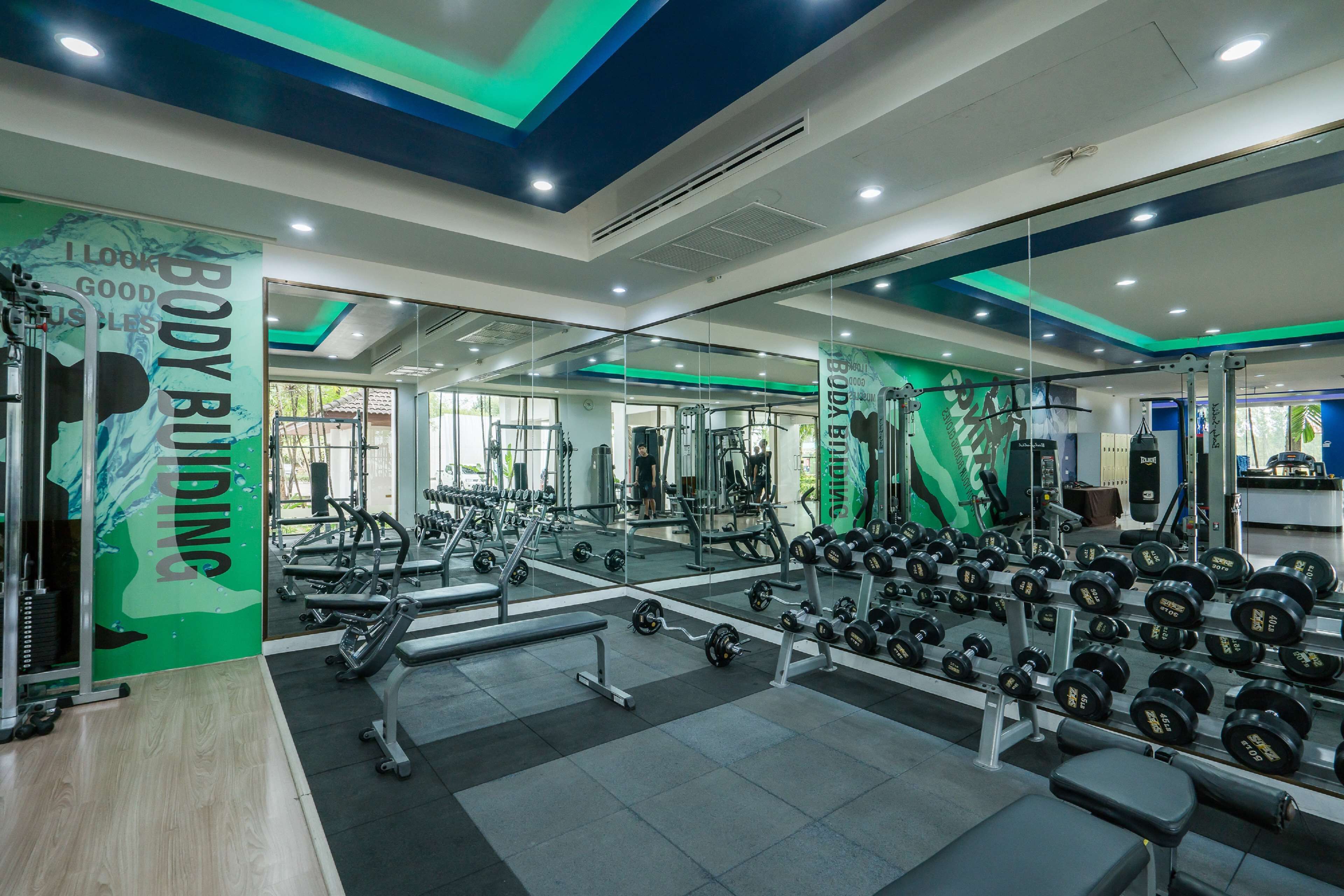 Un gimnasio con equipo de ejercicio variado, espejos y una pared verde con texto motivacional.