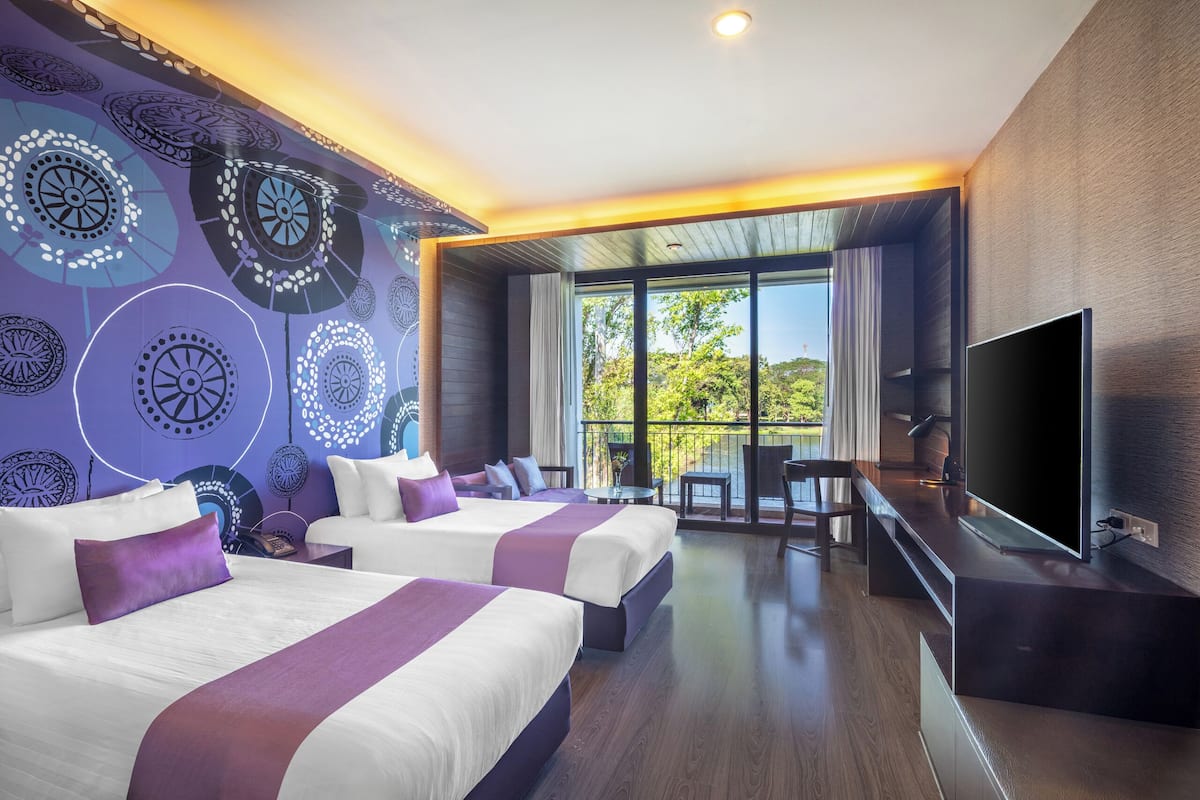 Ein modernes Hotelzimmer mit zwei Betten, einem Fernseher und einem Balkon mit Blick auf Grünflächen.