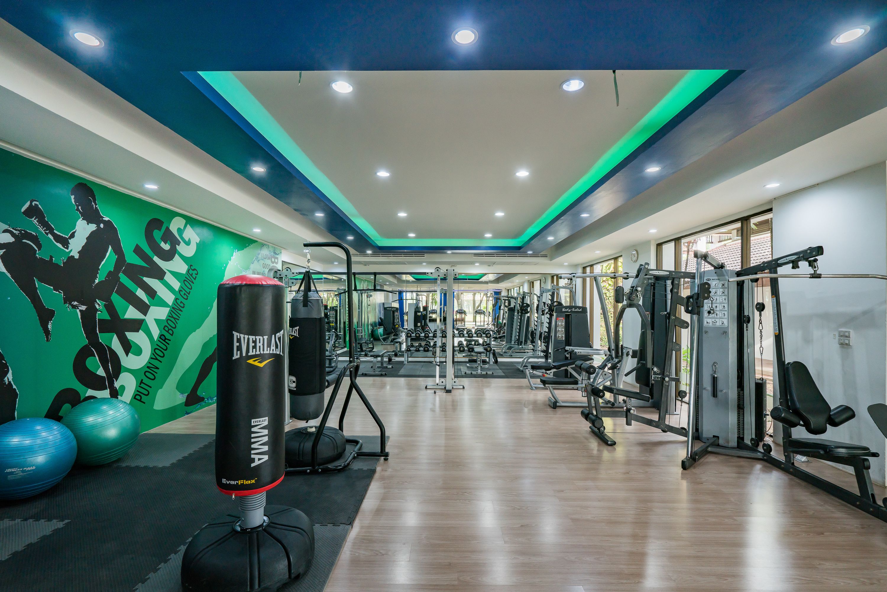 A gym with various exercise equipment, a punching bag, and a green wall with motivational text.
