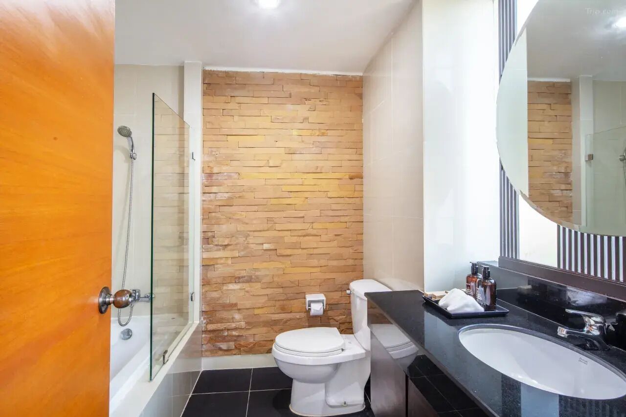 A bathroom with a glass shower enclosure, a white toilet, and a black sink with a large mirror above it.