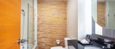 A bathroom with a glass shower enclosure, a white toilet, and a black sink with a large mirror above it.