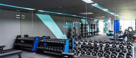 Un gimnasio moderno con diversos equipos de levantamiento de pesas, incluyendo mancuernas y bancos.