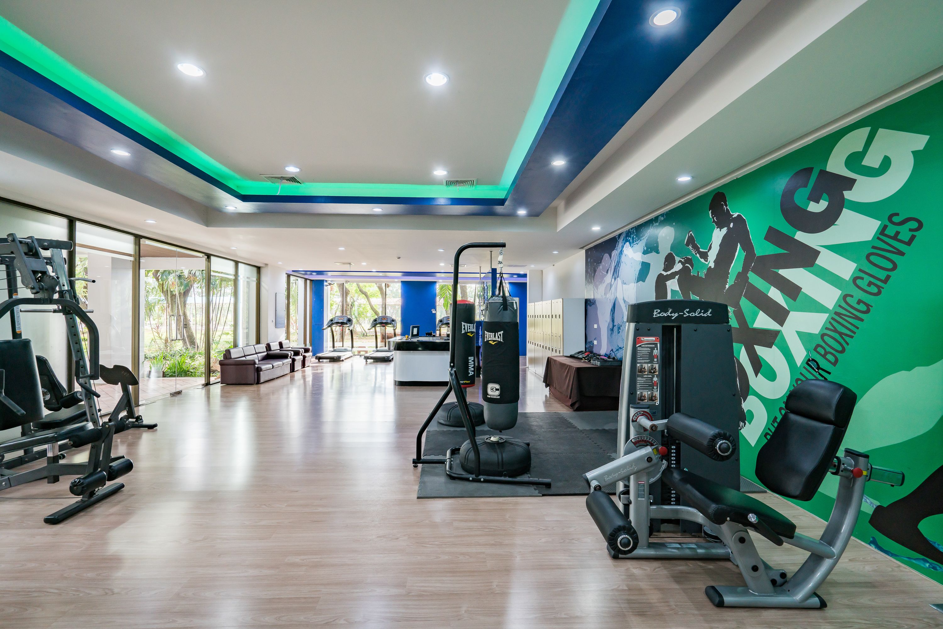 Un gimnasio con equipo de ejercicio variado, un saco de boxeo y una pared con publicidad de guantes de boxeo.