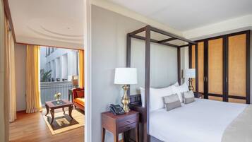 A hotel room with a large bed, a bedside table with a lamp, a small table with a phone, and a view of the outside balcony.