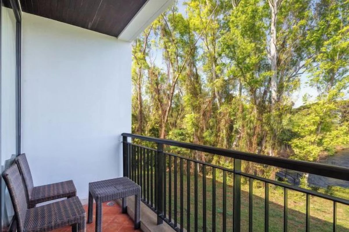 Varanda com móveis de vime e vista para uma área arborizada.