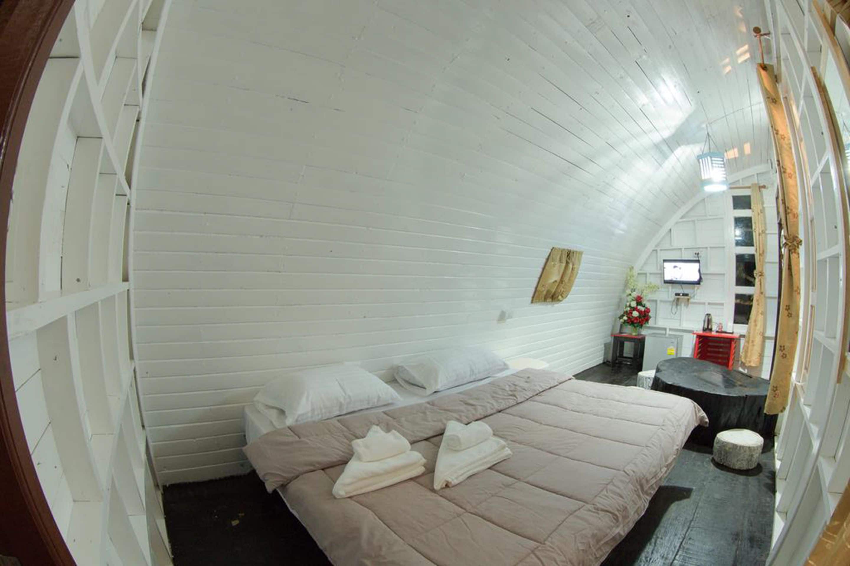 A room with a bed, a small table with a TV, and a window with curtains.