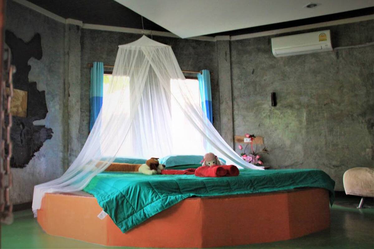Ein Zimmer mit einem Bett, einem Moskitonetz, einem Fenster mit Vorhängen und einer Klimaanlage.