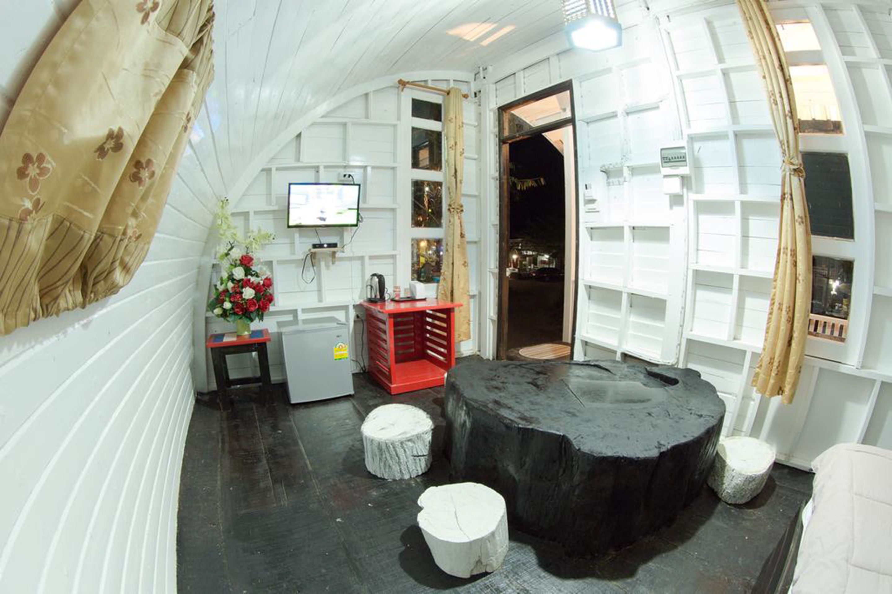 A room with a large black circular table, white walls, and a small TV on the wall.