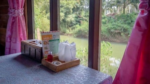 Una mesa con un menú, un vaso y una botella, y vistas a un río y vegetación al exterior.