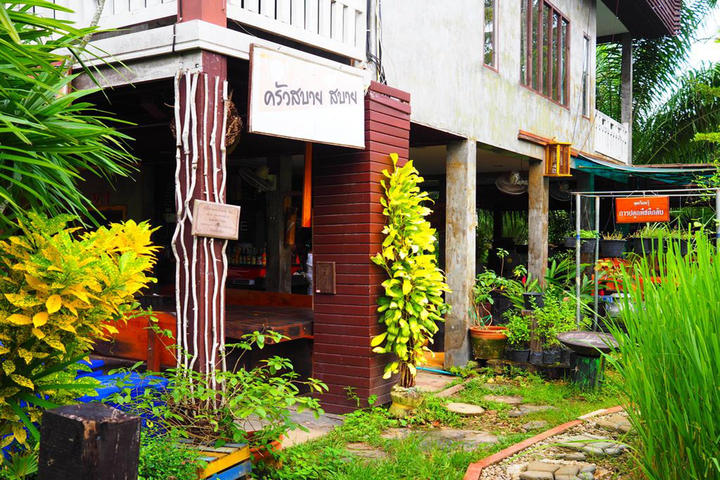 A building with a signboard, surrounded by lush greenery and potted plants.