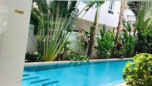 A swimming pool with clear blue water, surrounded by lush green plants and a white wall. - The Place Pratumnak by PSR ASIA (Pattaya)