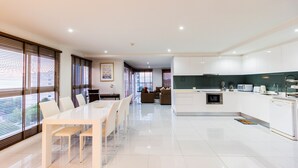 A modern kitchen with white cabinets, a microwave, and a sink. There is a dining area with a white table and chairs. - The Place Pratumnak by PSR ASIA (Pattaya)