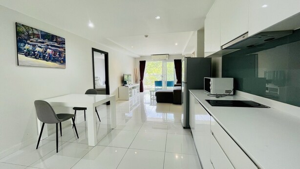 A modern kitchen with white cabinets, a dining area with a white table and chairs, and a large window with a view of greenery. - The Place Pratumnak by PSR ASIA (Pattaya)