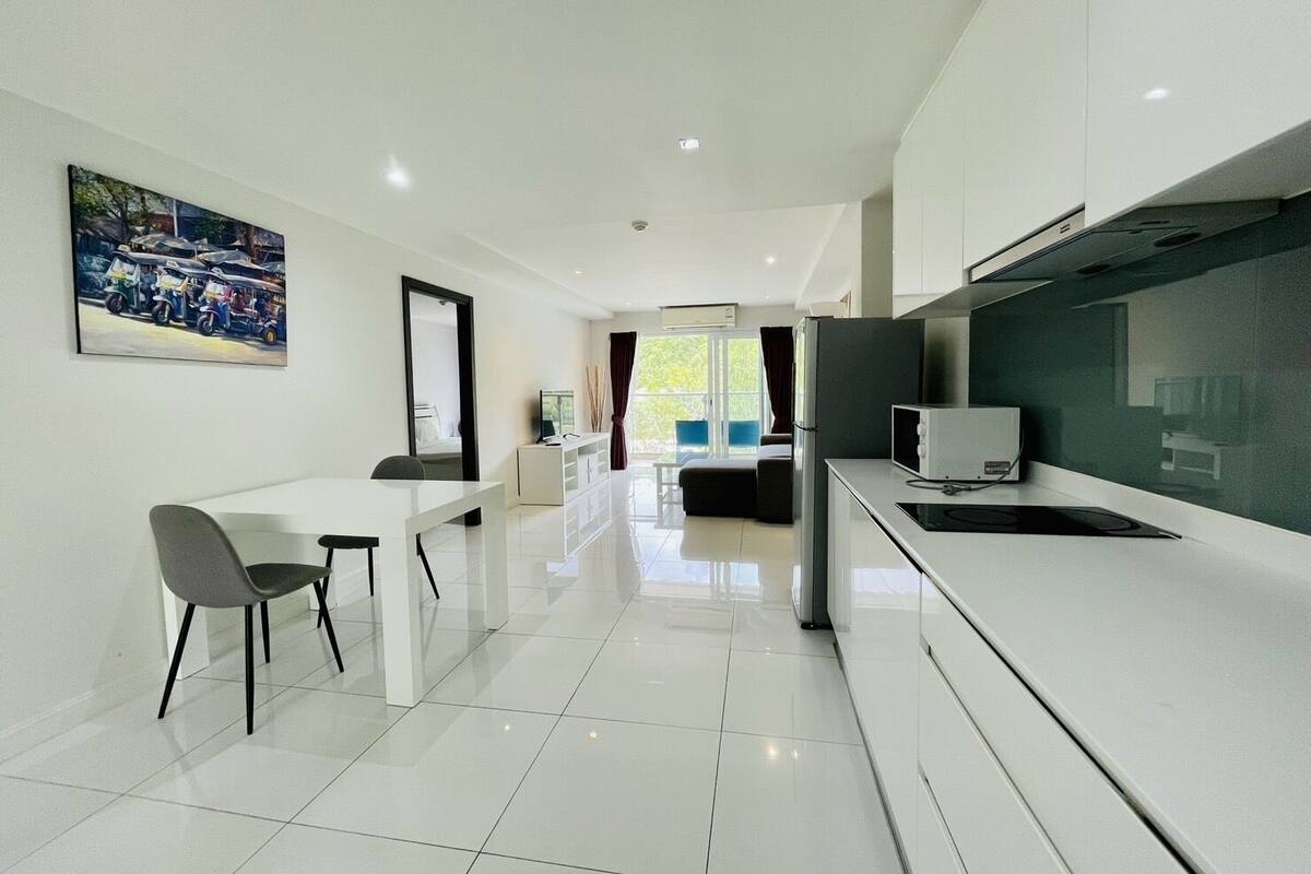 A modern kitchen with white cabinets, a dining area with a white table and chairs, and a large window with a view of greenery.