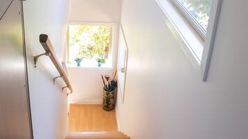 A staircase with a wooden handrail, a window with a view of greenery, and a hanging flower arrangement.
