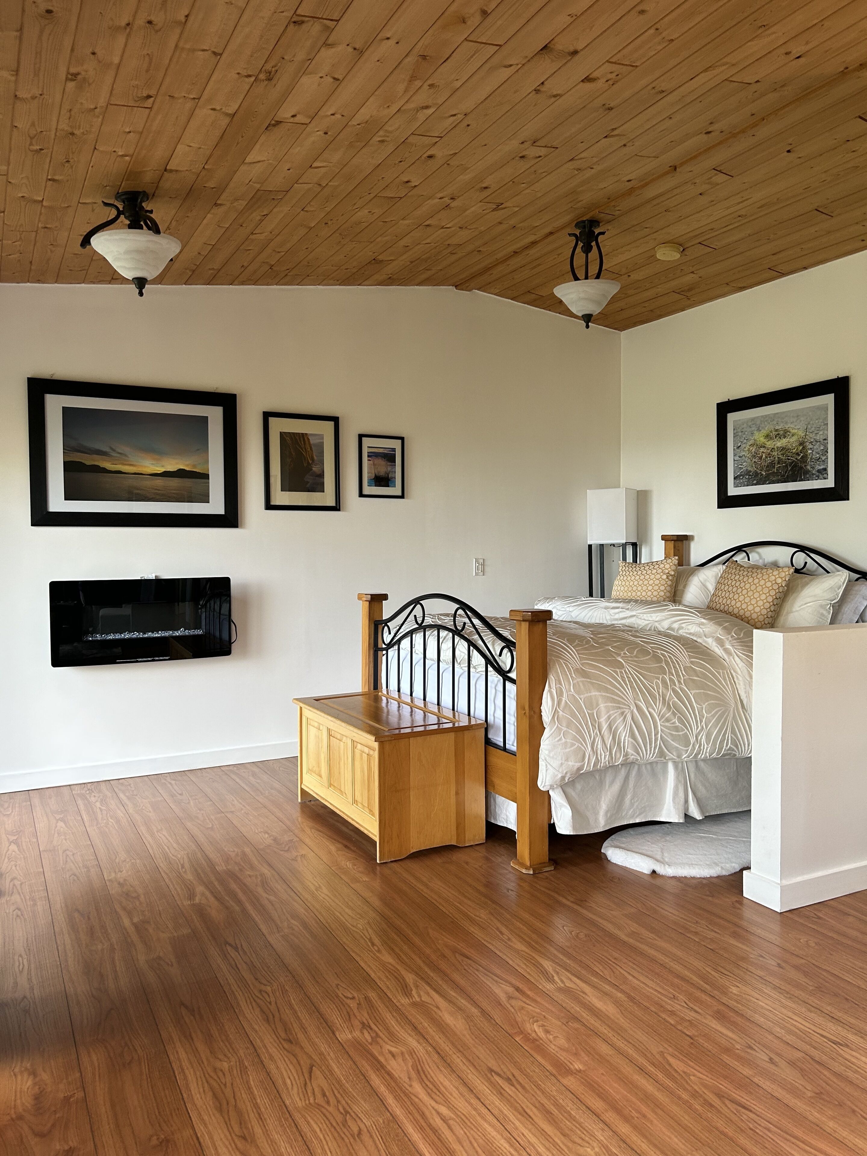 A bedroom with a wooden ceiling, a bed with patterned bedding, a bedside table, and wall-mounted artwork.