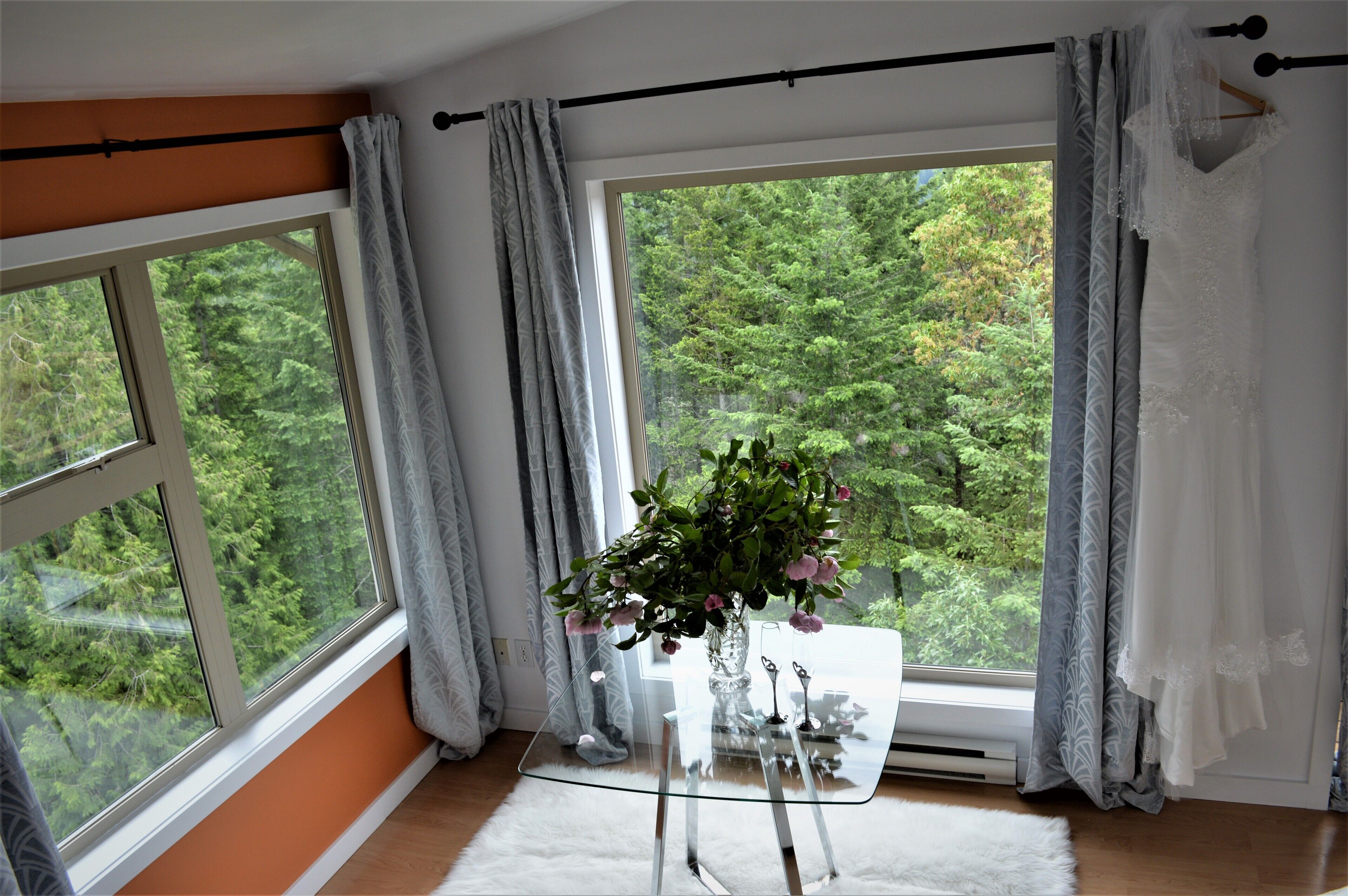 Una habitación con un ventanal grande, una mesa de vidrio con un florero y un manto de piel blanca.