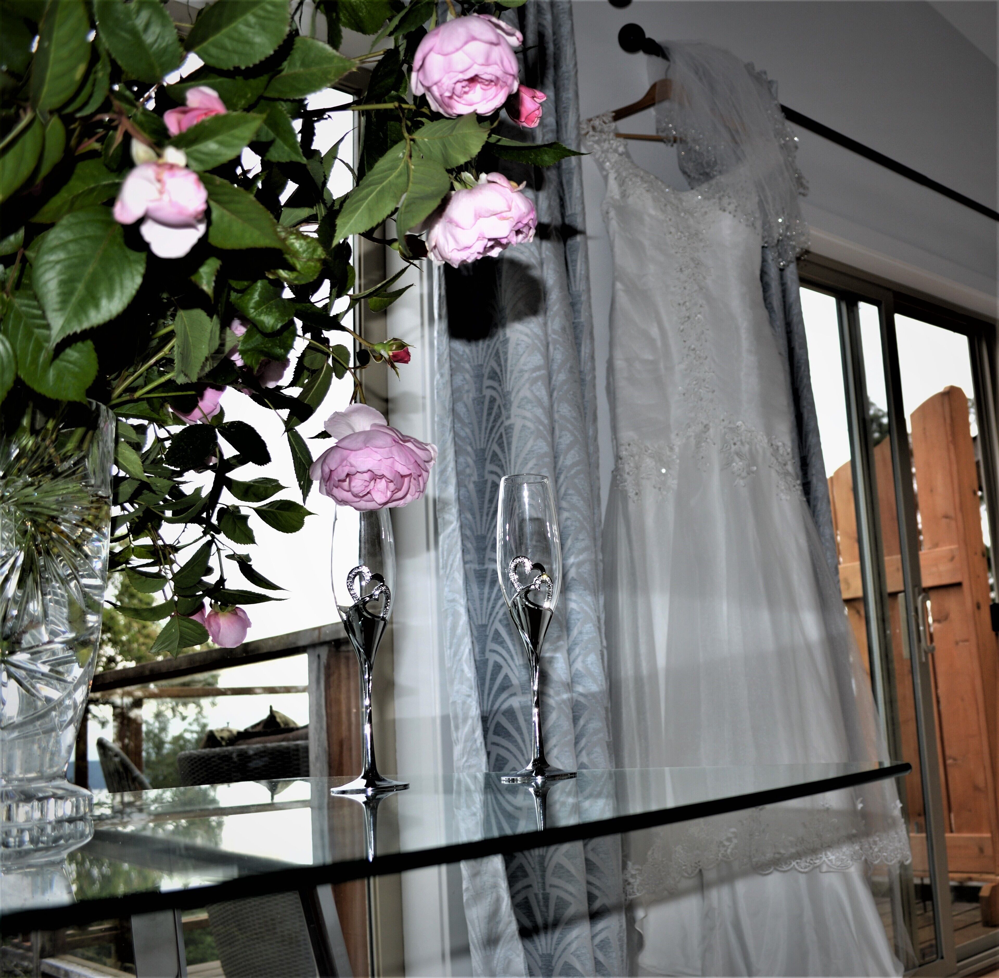A room with a large window, a glass table, and a vase with pink flowers.