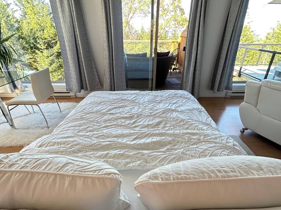 A bedroom with a large bed, a balcony with a chair, and a view of trees.