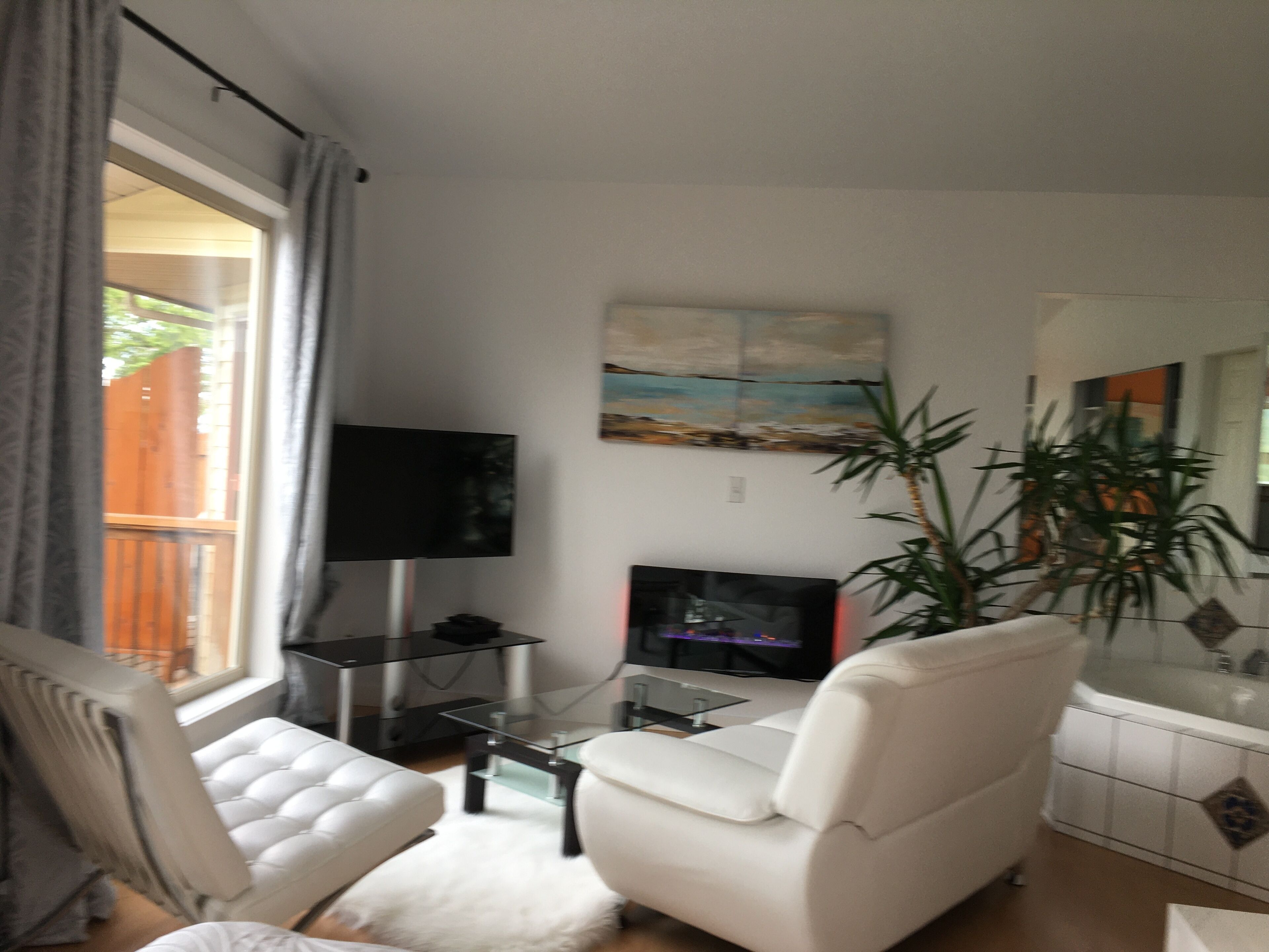 Ein Wohnzimmer mit einem weißen Sofa, einem Flachbildfernseher, einem kleinen Tisch und einer Topfpflanze.