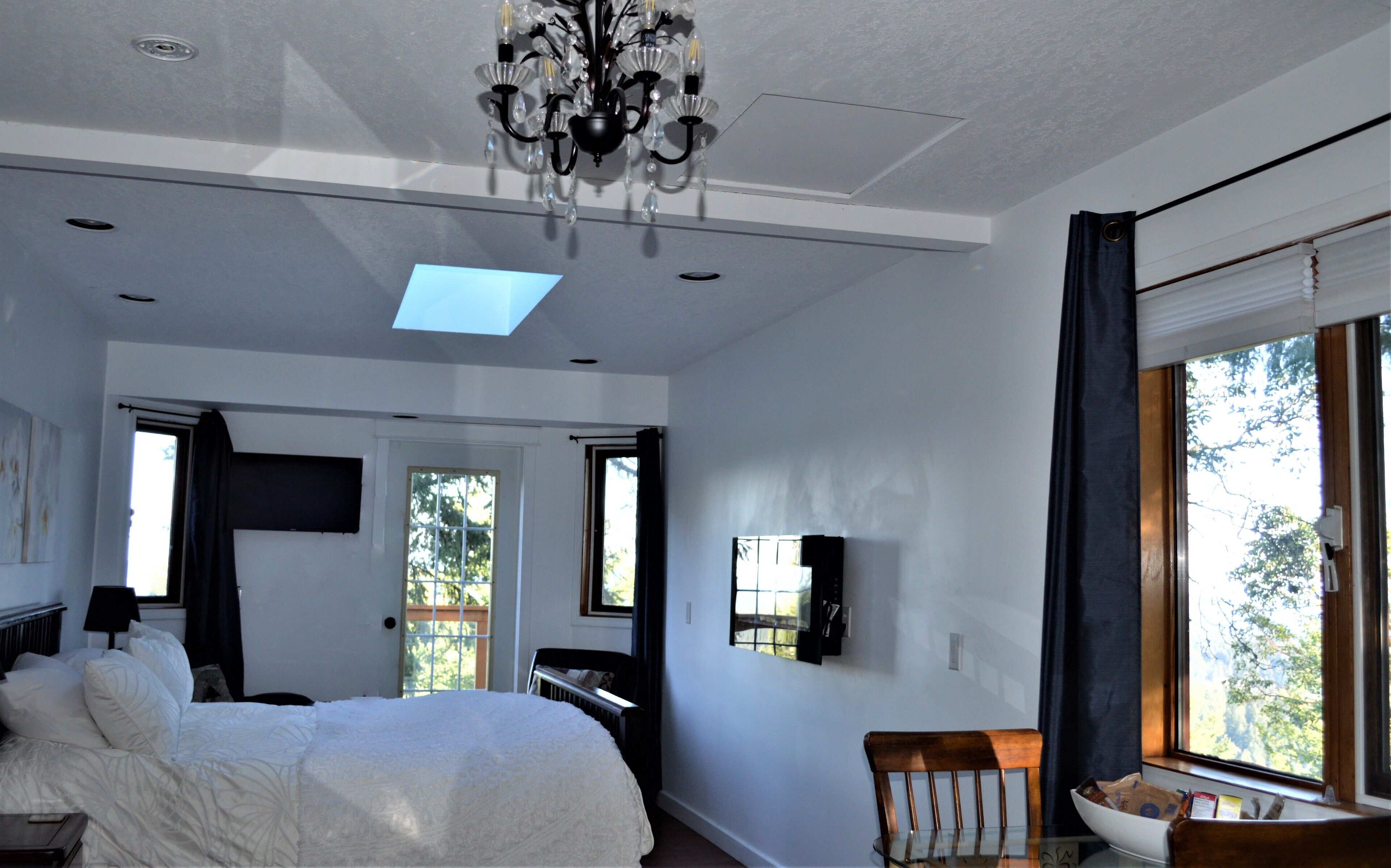 A bedroom with a large bed, a chandelier, a television, and a window with curtains.