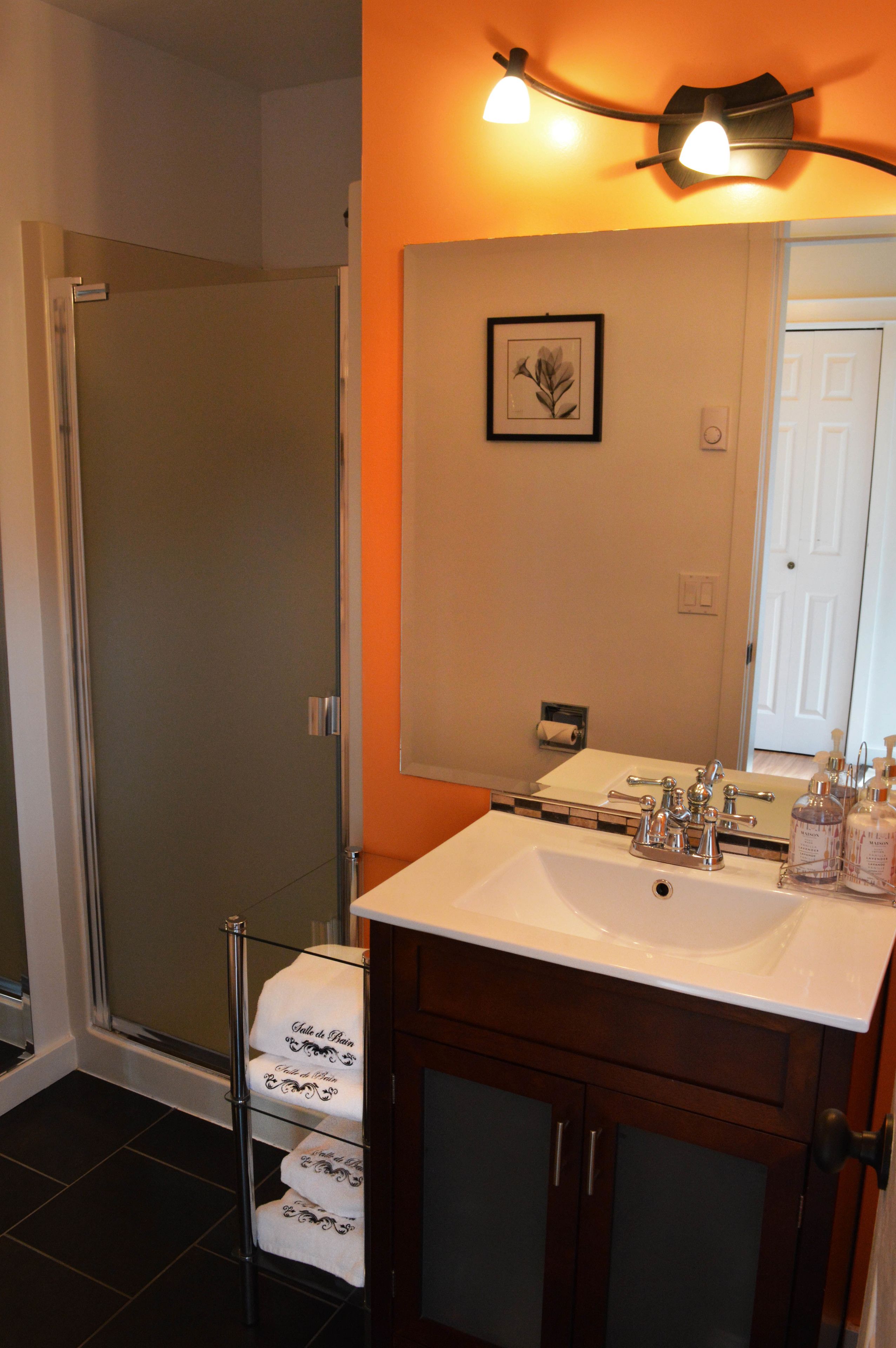 A bathroom with a glass shower enclosure, a white sink with a mirror above it, and a towel rack with towels.