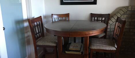 Un coin repas avec une table ronde et quatre chaises en bois, un tableau encadré au mur et une cheminée en pierre.