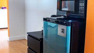 A compact kitchen with a built-in microwave and refrigerator, wooden flooring, and a white wall with a window.