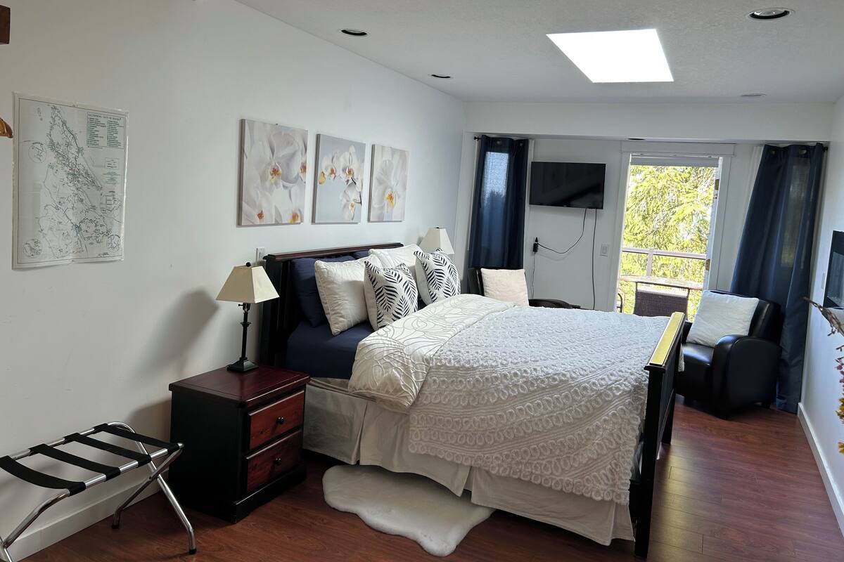 A bedroom with a bed, bedside tables, a desk, a chair, and a view of the outdoors.