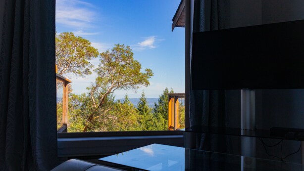 A room with a large window offering a view of trees and a building. - Elevate Rooms Armand Heights (Salt Spring Island)
