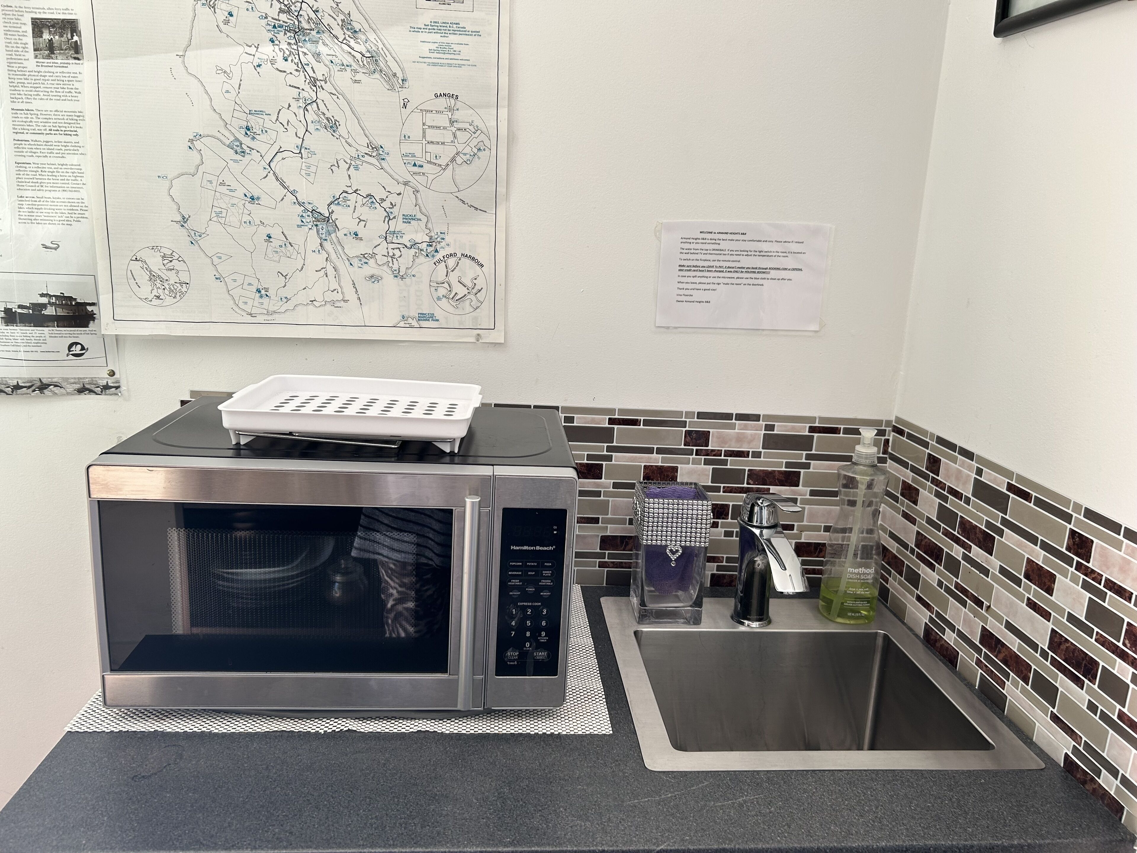 Een keuken met een roestvrijstalen magnetron, een spoelbak en een betegelde spatwand.