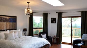 A bedroom with a large bed, a chandelier, a desk, and a view of the outdoors.