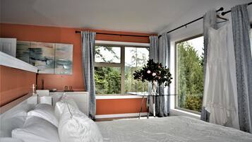 Un dormitorio con una cama grande, una ventana con cortinas, una mesita de noche con un florero y un cuadro en la pared.