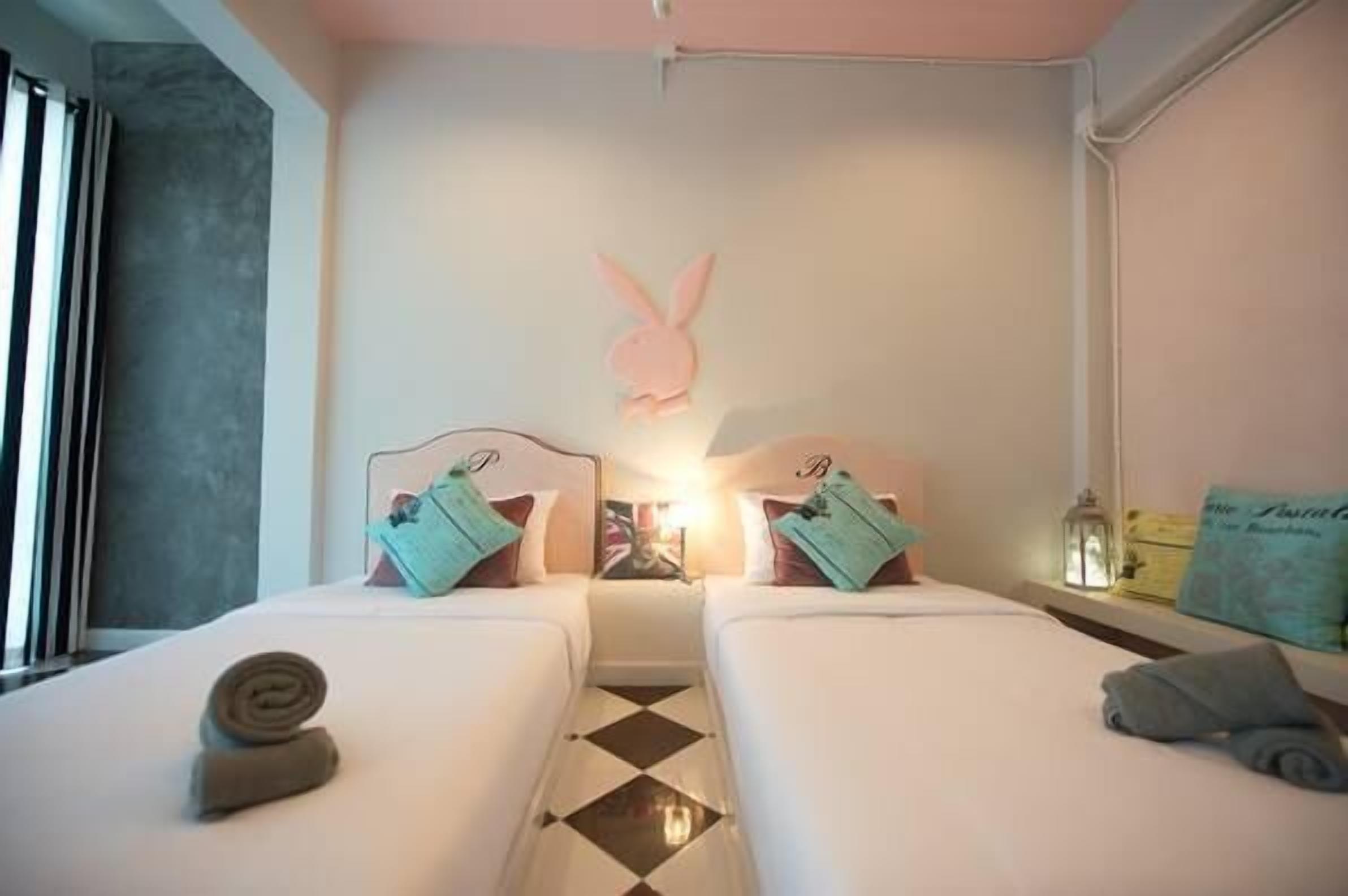 Habitación de hotel con dos camas, un conejo decorativo en la pared y suelo a cuadros.